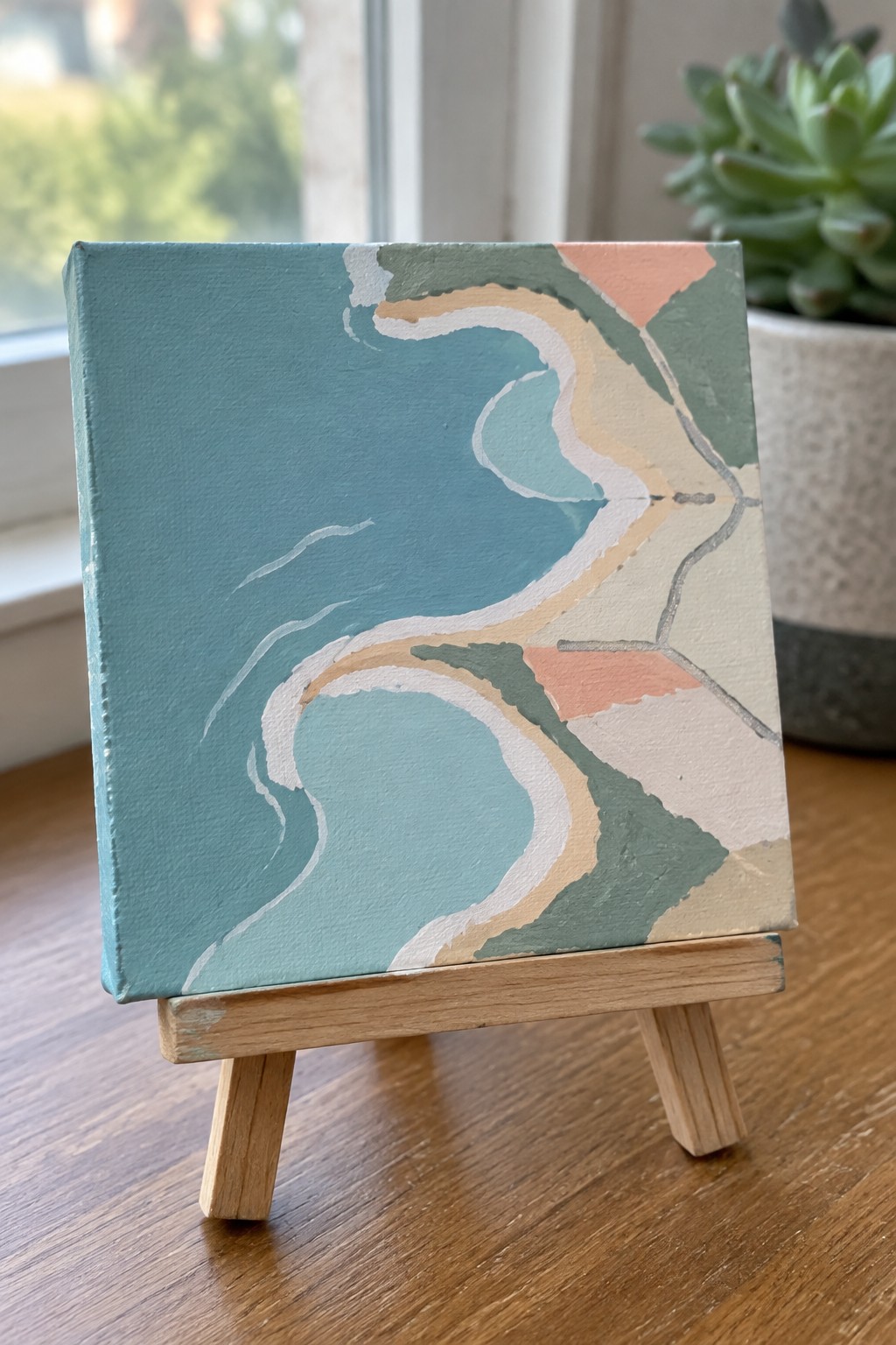 Abstract teal painting with wavy shapes on miniature wooden easel beside succulent plant