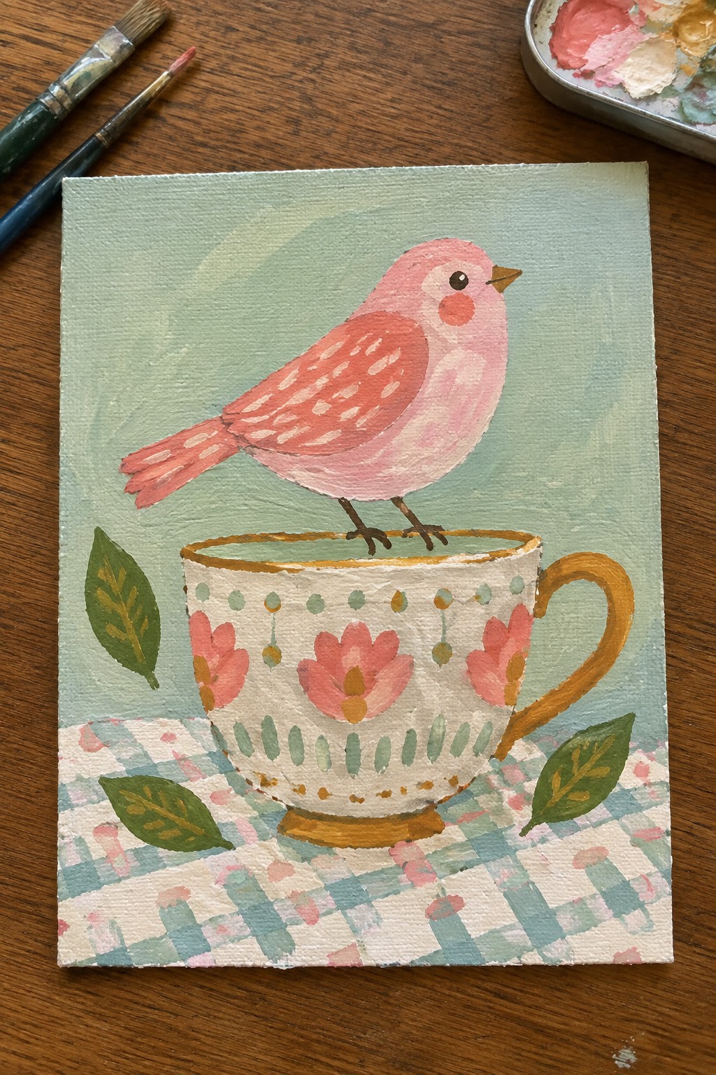 Pink bird perched on floral teacup atop checkered cloth with green leaves