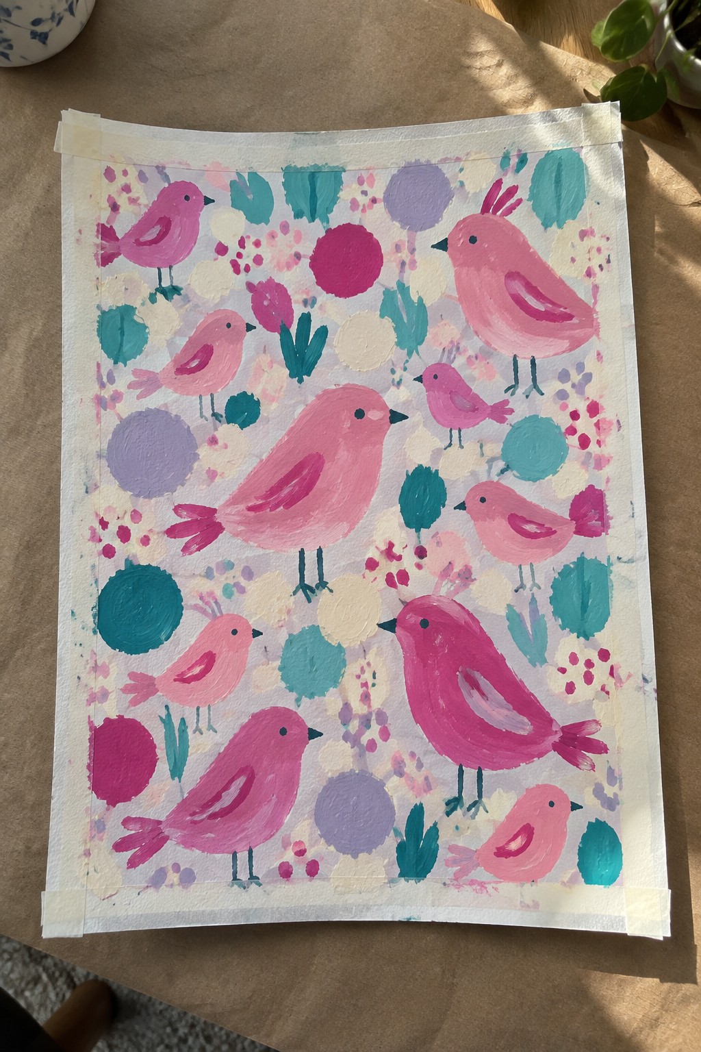 Pink birds amid colorful circles, leaves, and dots on taped paper painting