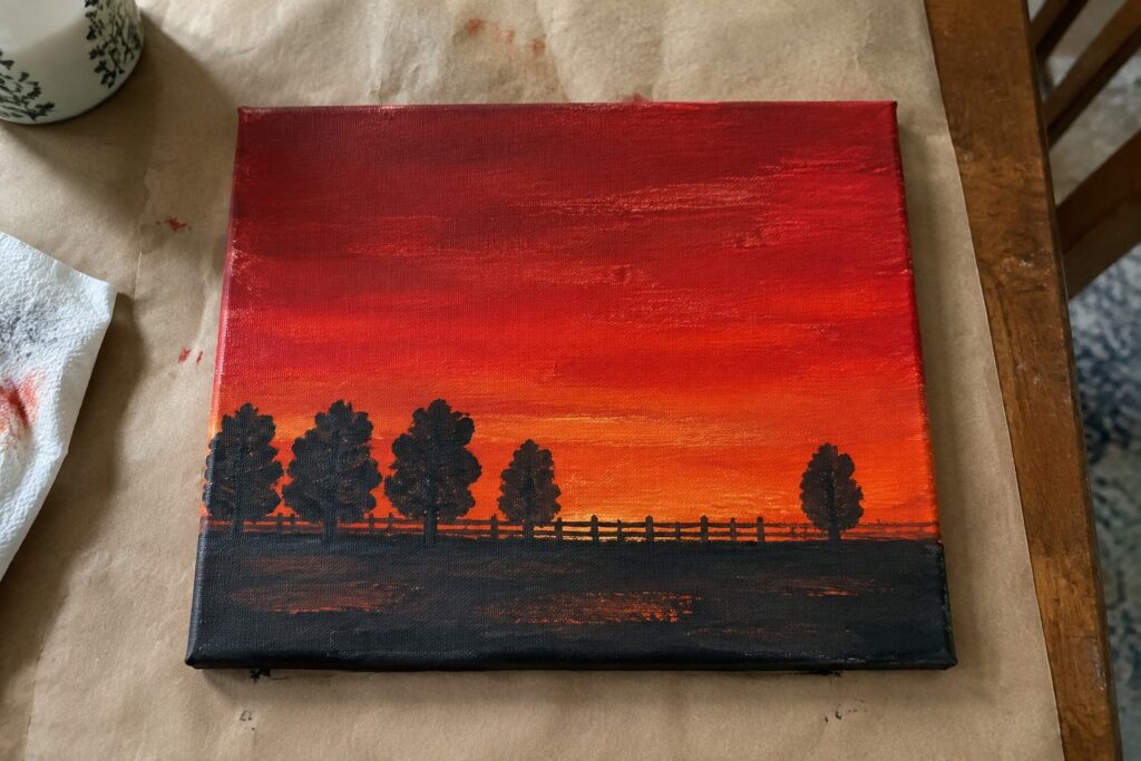 16 Rich Red Sunset Acrylic Painting Ideas With Dark Foreground Shapes Canvas painting of vibrant red-orange sunset with black tree silhouettes and fence.