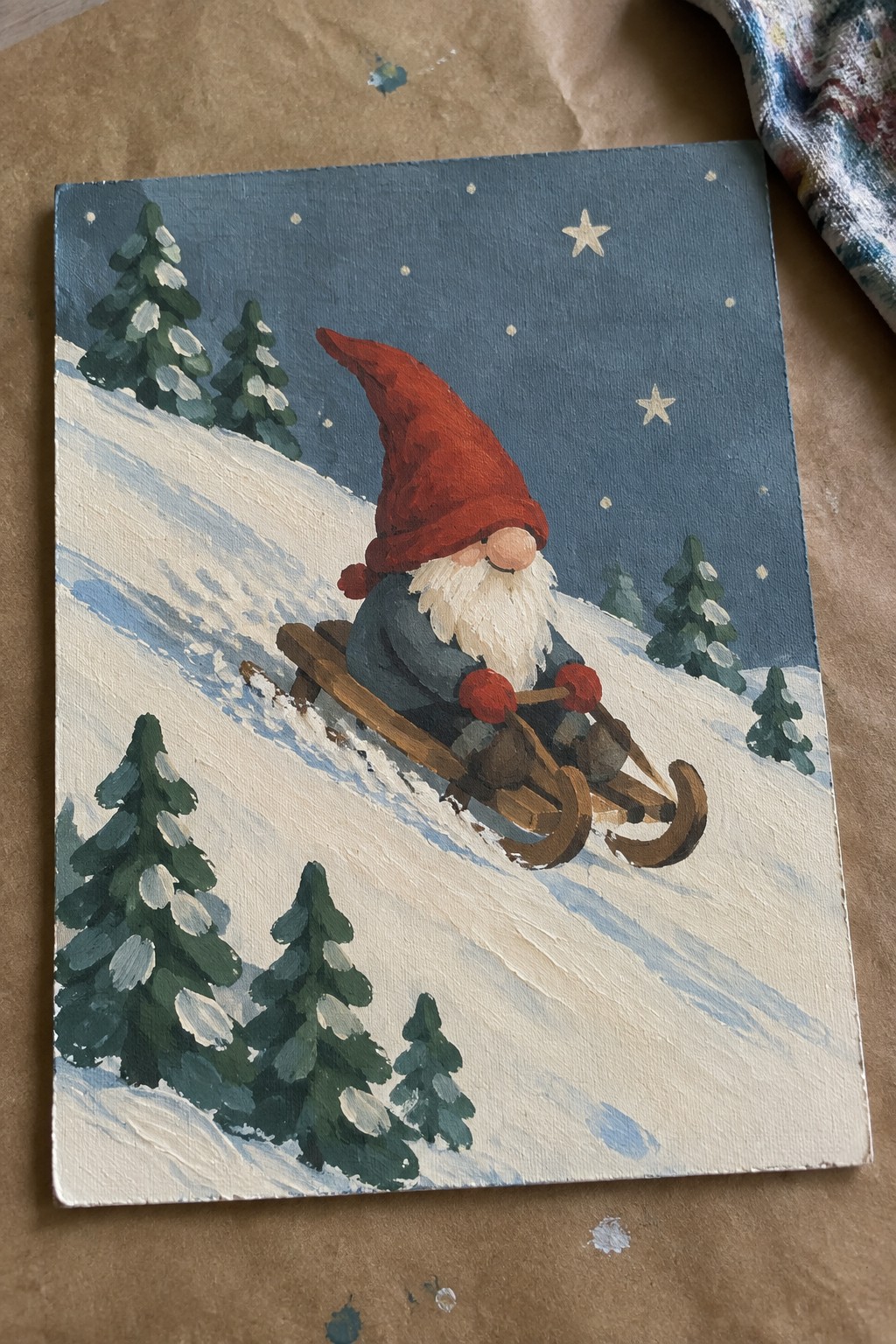 Gnome in red hat and blue coat sledding down snowy hill with pine trees at night