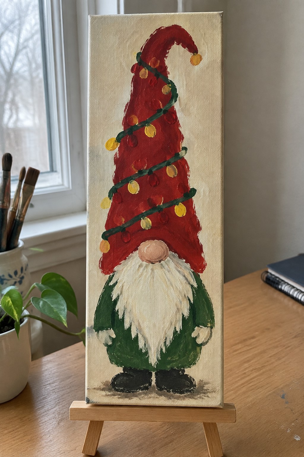 Christmas gnome painting with red hat, white beard, green coat and string lights on easel