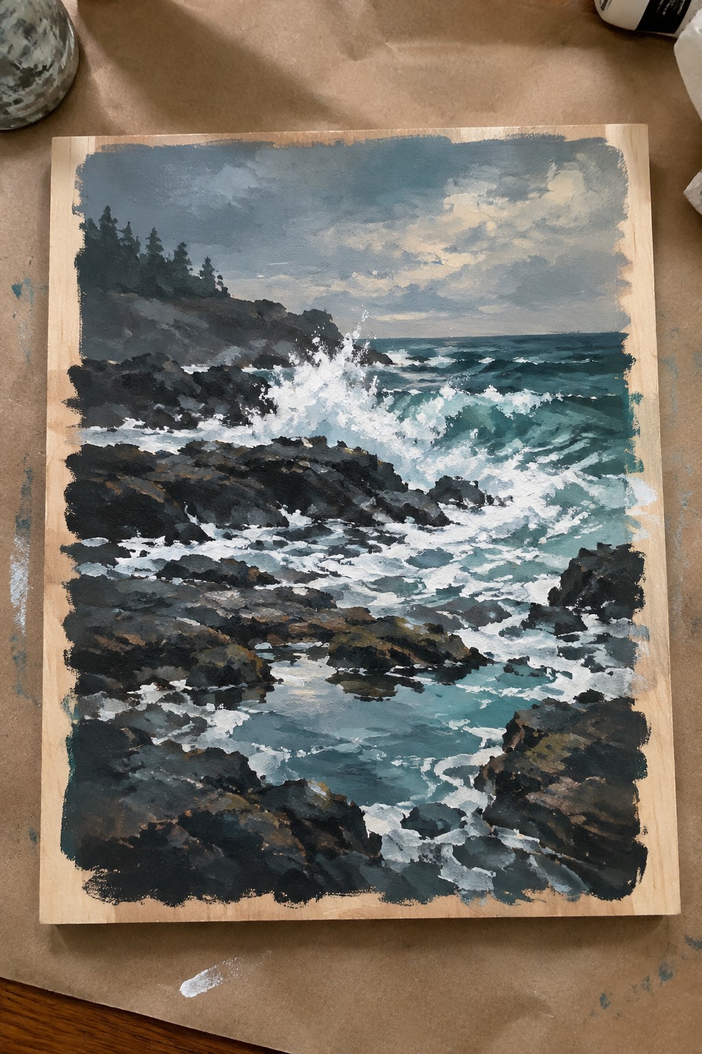 Seascape painting of crashing white waves on dark rocks under cloudy sky with trees