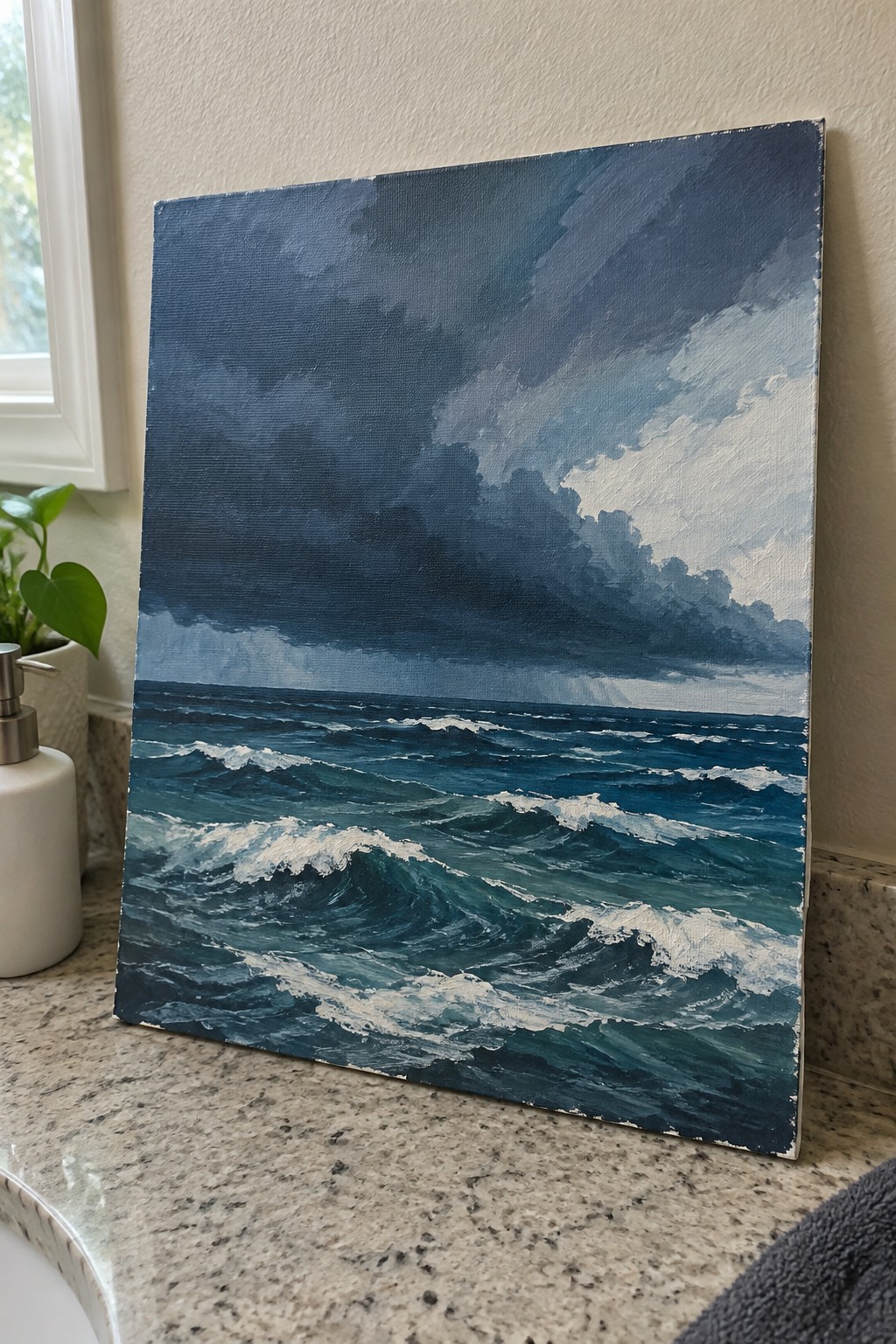 Seascape painting of stormy dark blue ocean with whitecaps on granite countertop beside plant