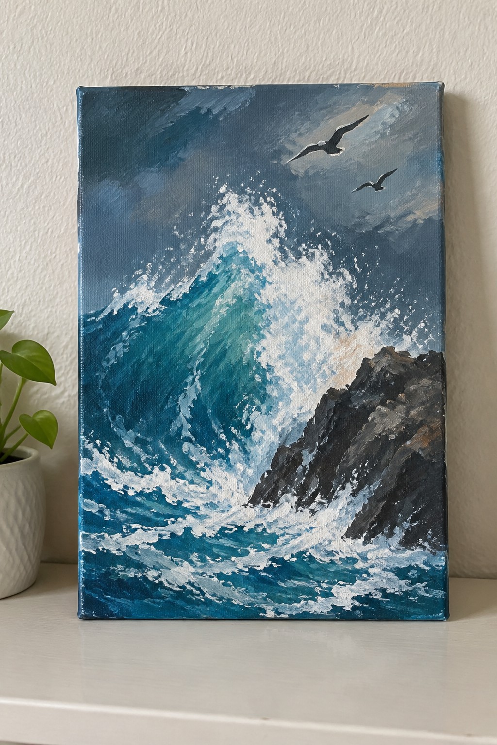 An acrylic painting of a large blue wave crashing against dark rocks with two birds flying overhead in a stormy sky.