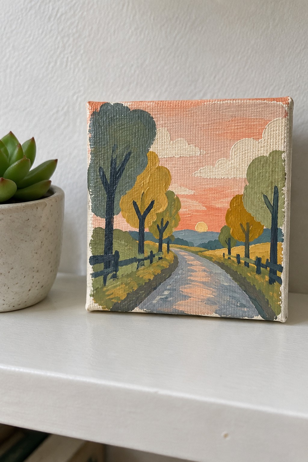 Small square painting of winding autumn road under orange sunset beside succulent
