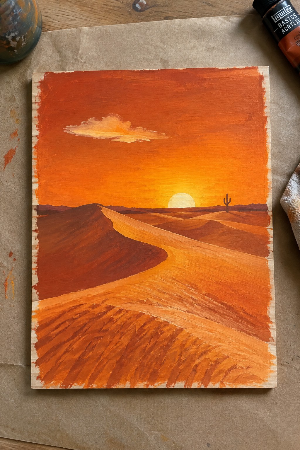 Acrylic painting of a desert sunset with rolling orange dunes, a setting sun, one cactus, and a single cloud in the sky.