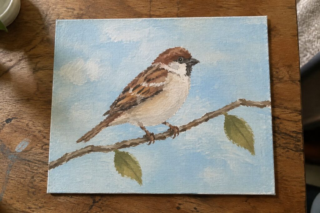 Sparrow with brown head perched on branch with green leaves against blue sky