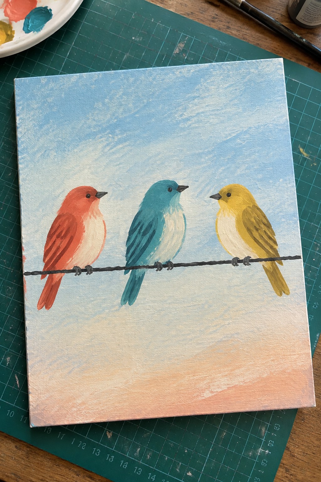 Three colorful birds perched on a wire against a blue sky with peach horizon