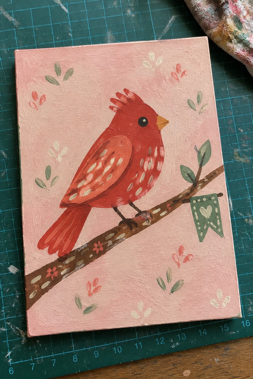 Red cardinal perched on branch against pink background with green heart banner.