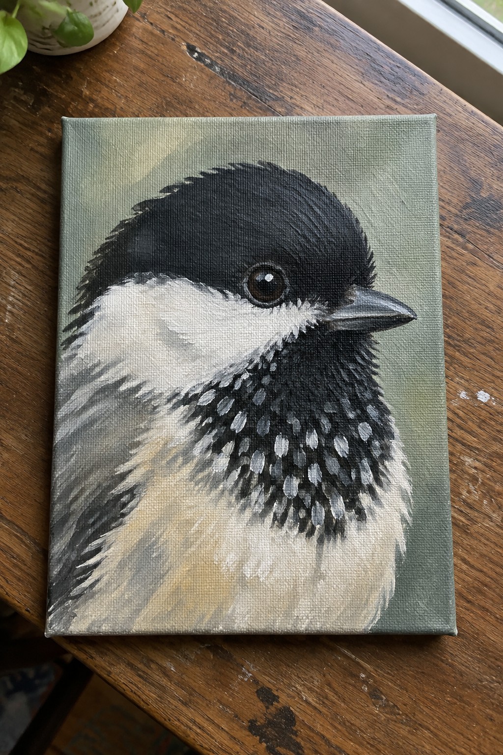 Canvas painting of chickadee with black cap on wooden table