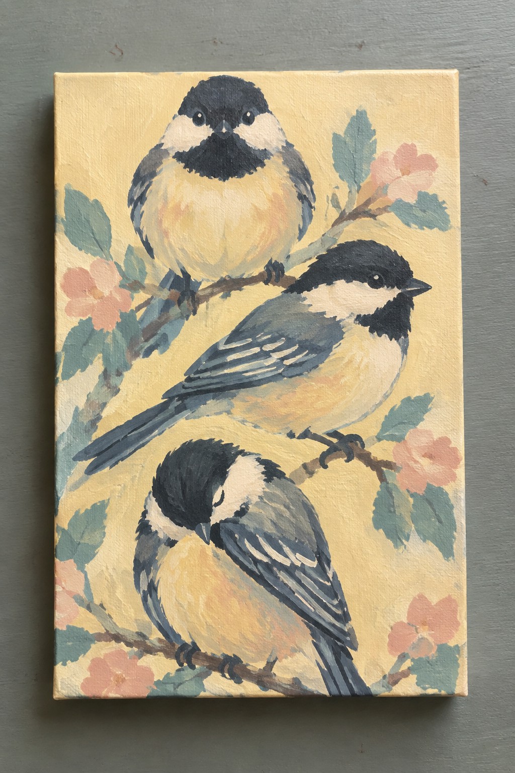 An acrylic painting of three chickadees on branches with pink flowers against a pale yellow background.