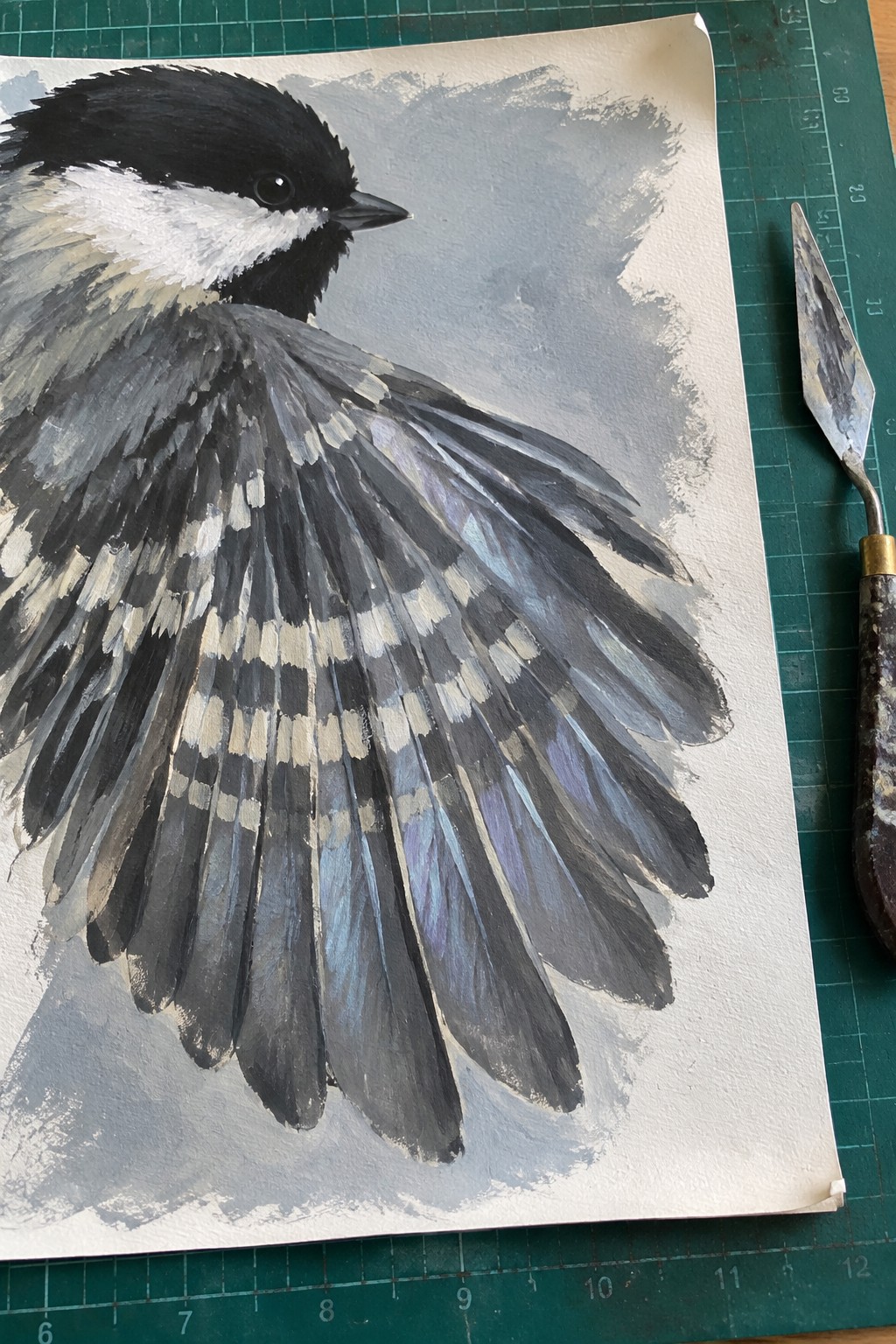 Painting of chickadee head and spread wing with palette knife on green mat