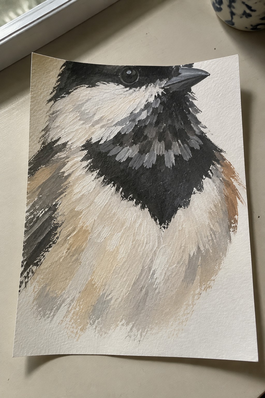 Close-up acrylic painting of a chickadee showing black head, white cheek patches, dark bib, and textured gray-brown feathers on white paper.