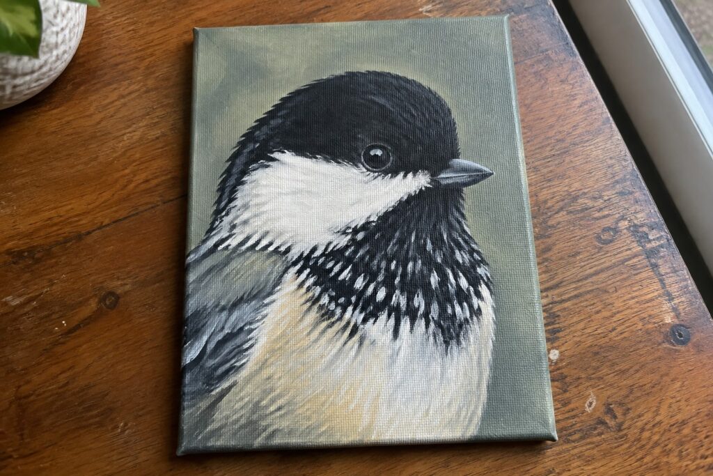 Canvas painting of chickadee with black cap on wooden table