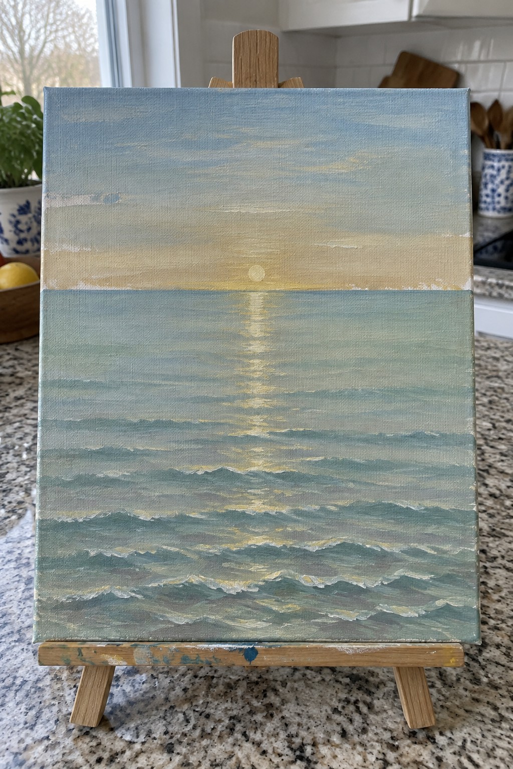 Seascape painting on wooden easel with blue ocean waves reflecting golden sunlight.