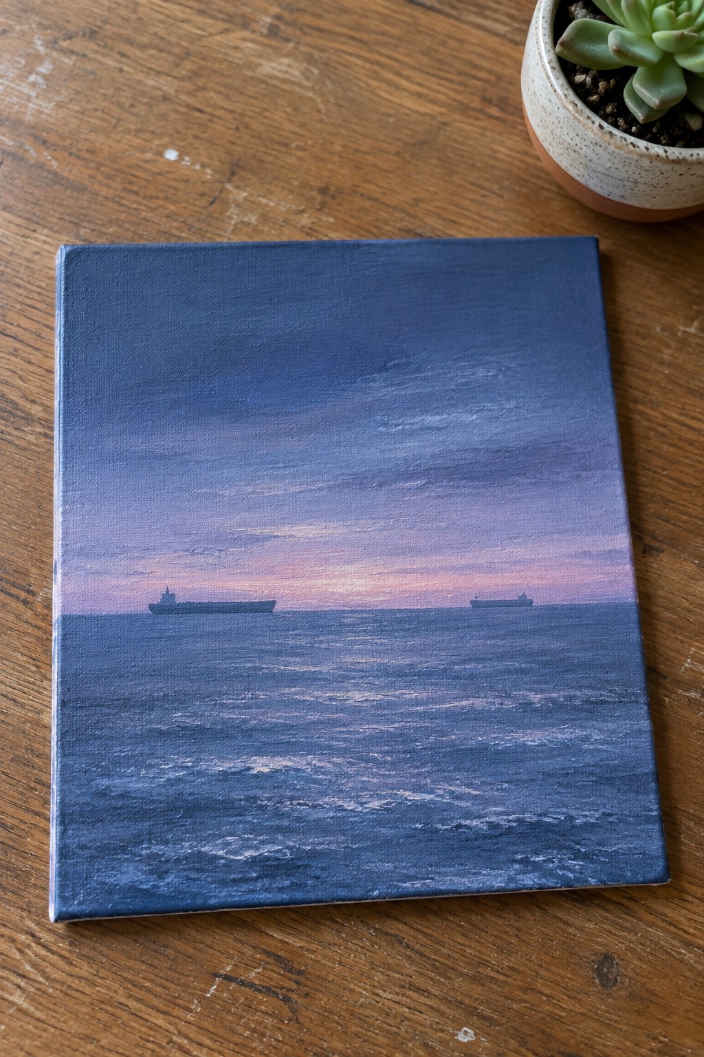 Seascape painting of two ships on blue sea under pink-purple sky beside succulent plant