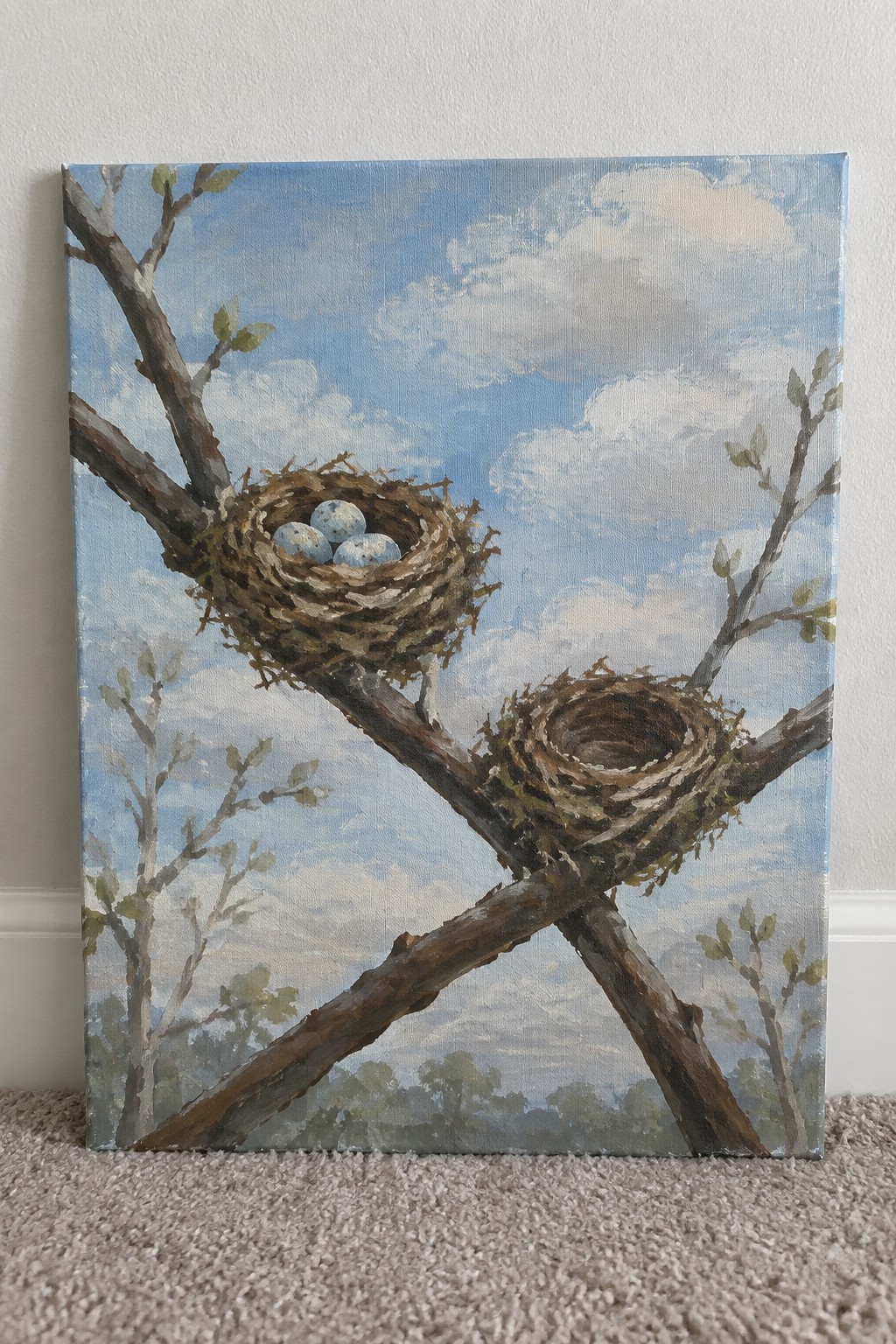 Two bird nests on intersecting branches, one with three blue eggs, under cloudy sky.