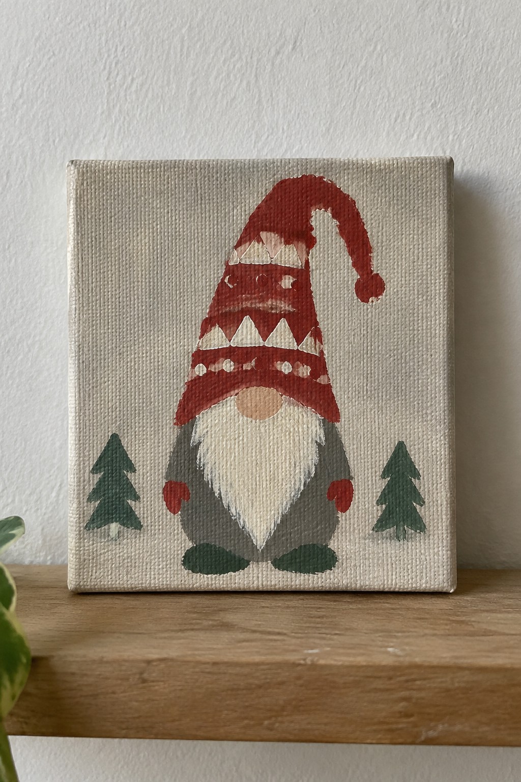 Gnome in red patterned hat with white beard and mittens between two green trees