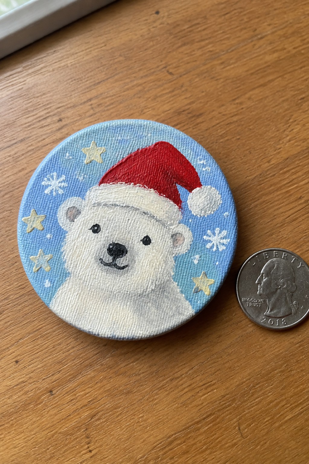 Painted polar bear in red Santa hat on blue starry canvas beside US quarter