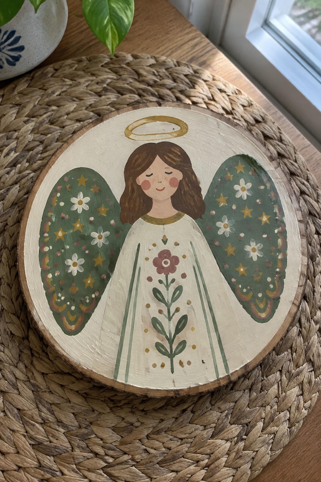 Hand-painted angel with halo, floral white dress, and starry green wings on wood slice