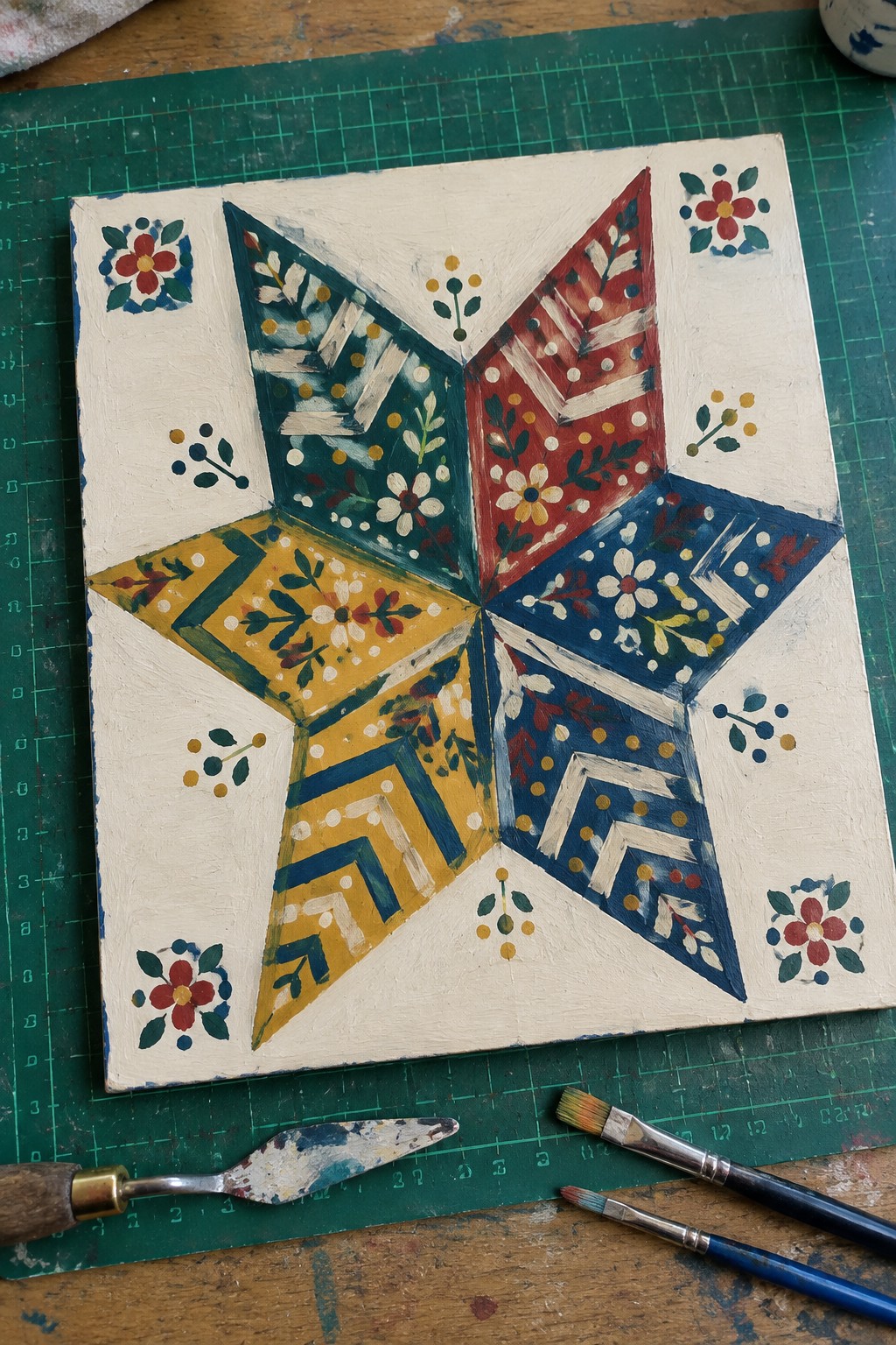Colorful hand-painted folk art star with floral patterns on white board beside brushes