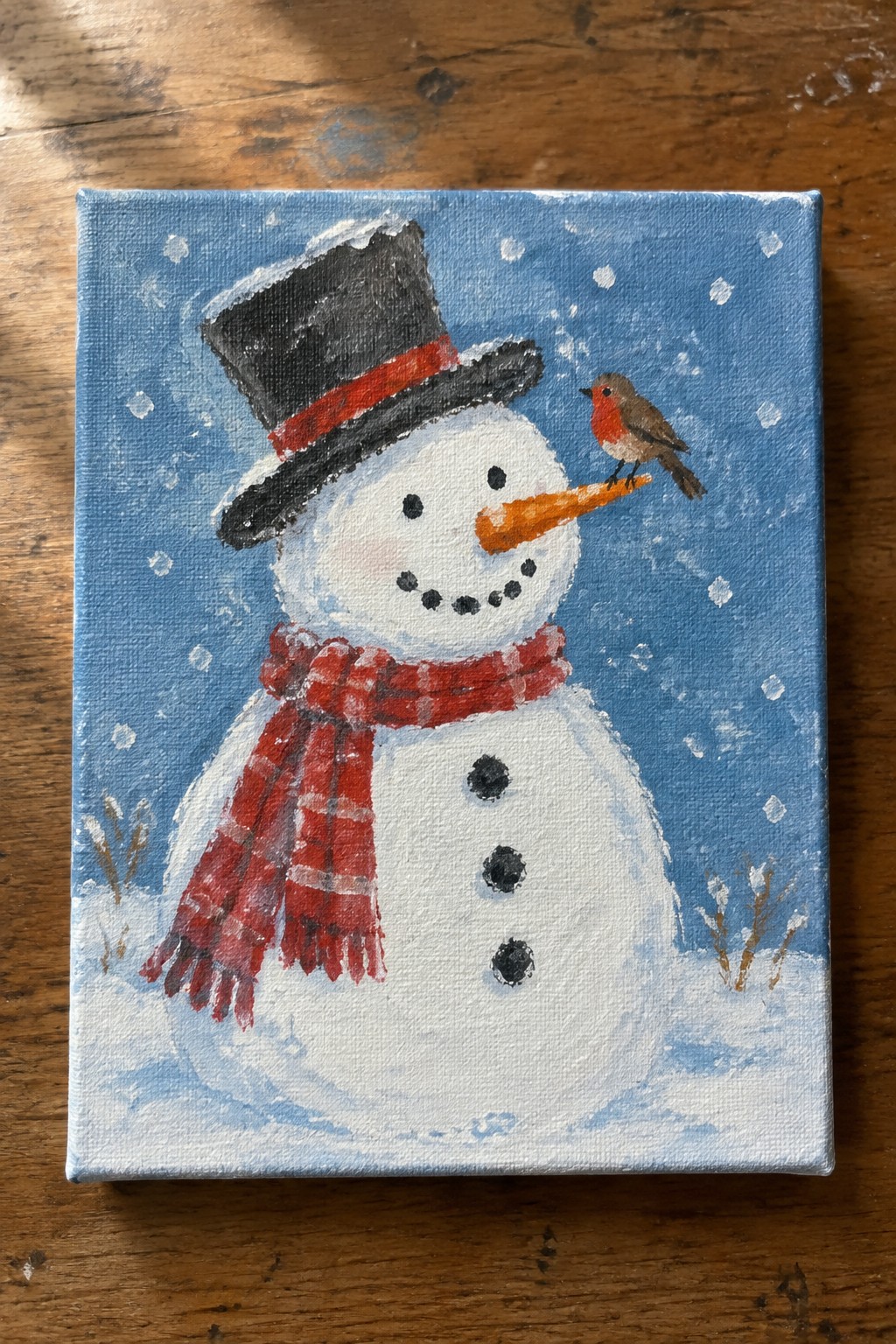Snowman in black top hat and red plaid scarf with robin on carrot nose