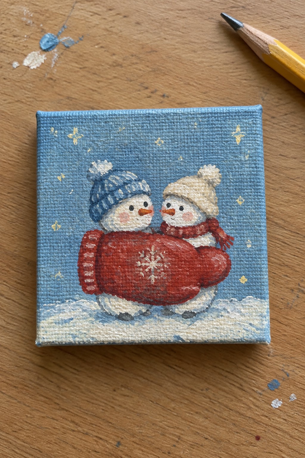 Two snowmen in winter hats share a red mitten on snowy canvas with stars