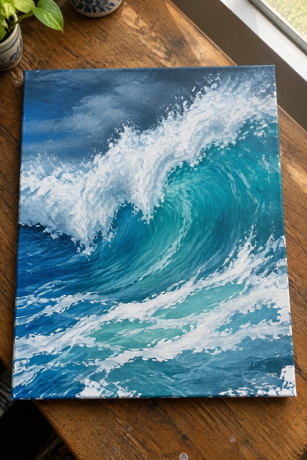 Ocean wave painting in blue and turquoise with white foam on wooden table