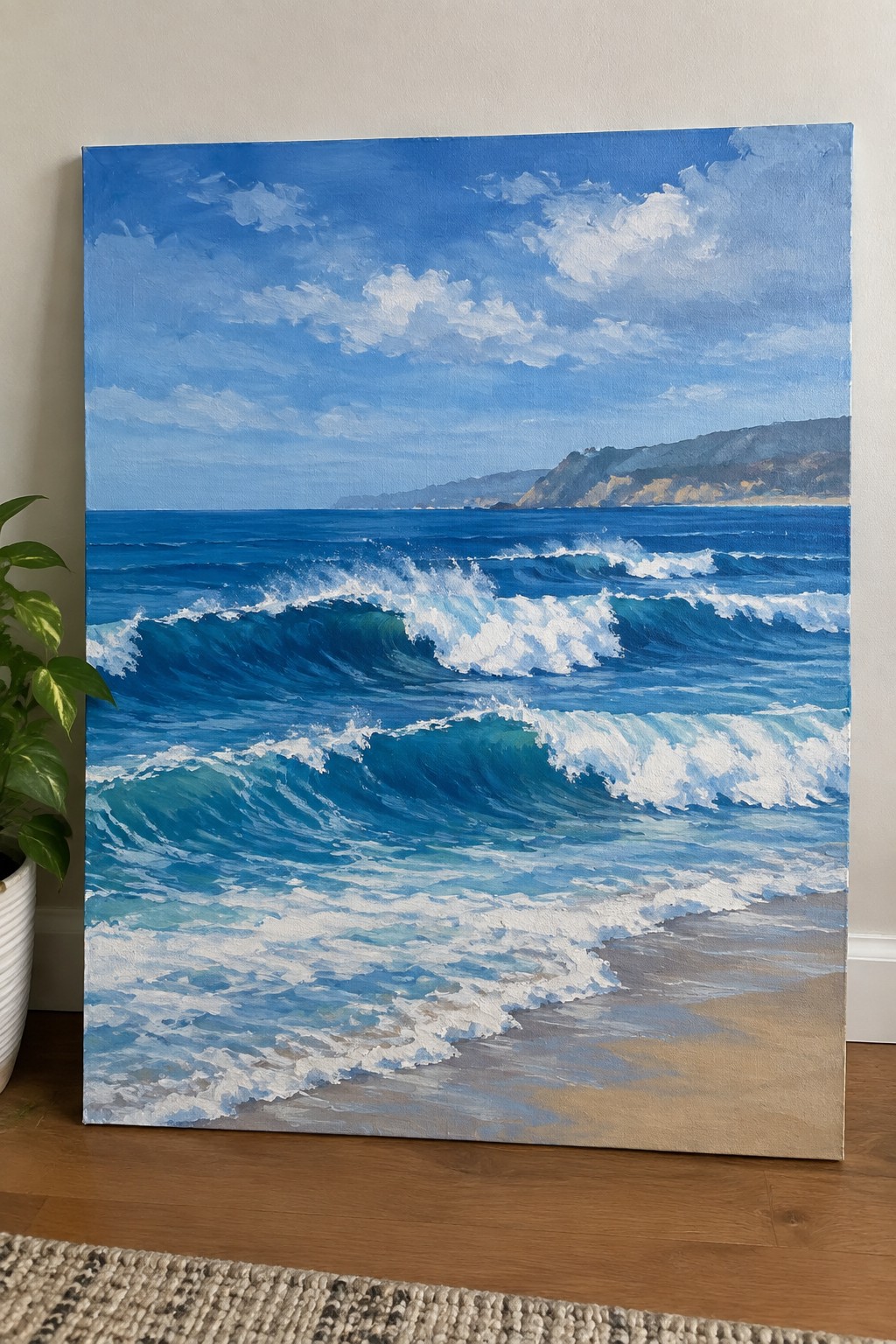 Seascape painting of blue waves crashing on sandy beach beside potted plant on floor