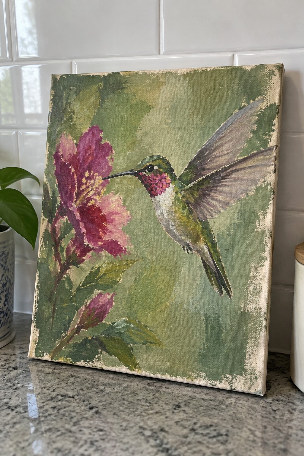 An acrylic painting of a hummingbird with spread wings hovering next to a pink flower on a green background.