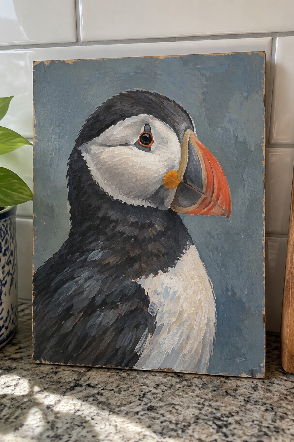 Acrylic painting of puffin with black feathers, white face, and bright orange beak on blue background