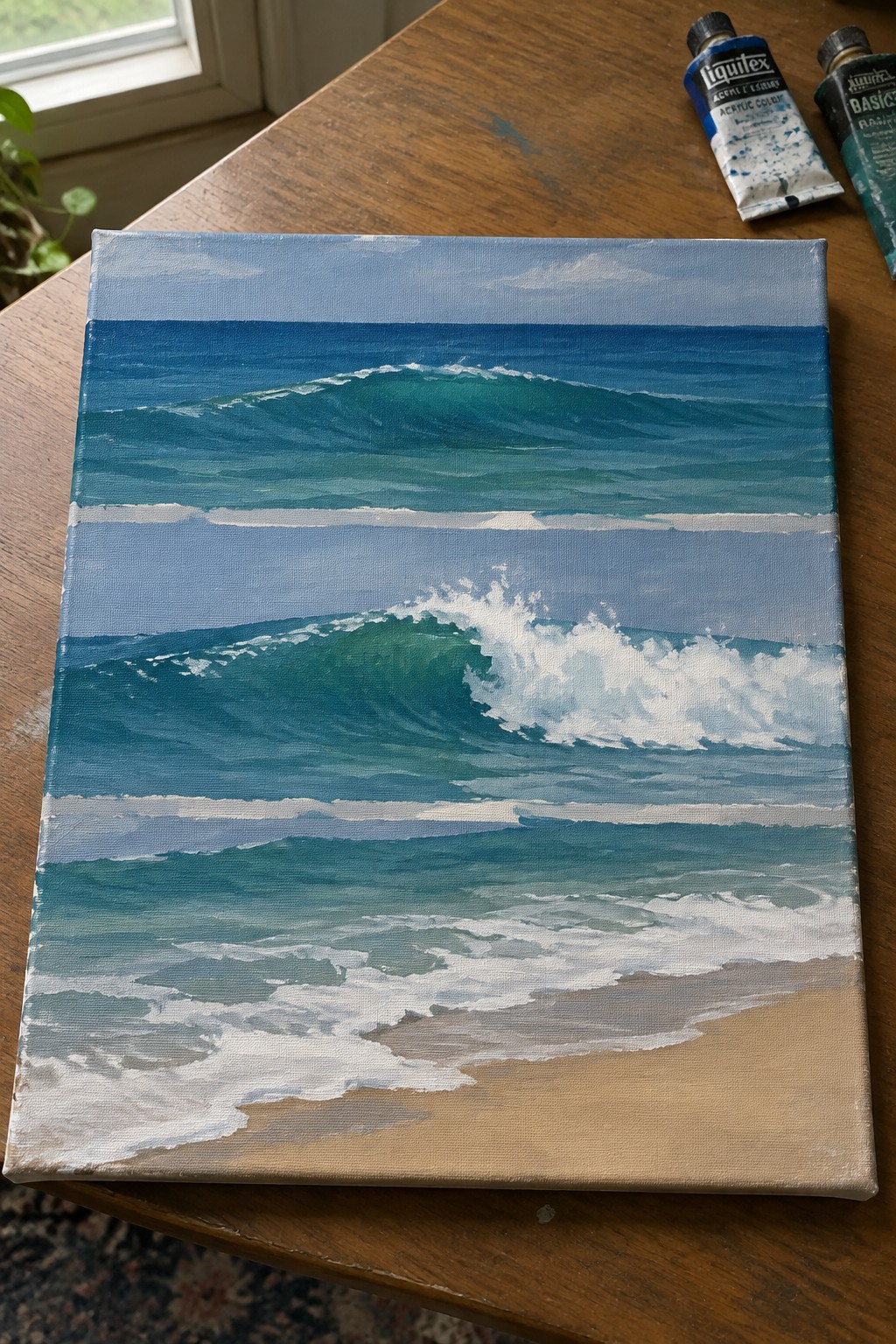 Canvas painting of turquoise waves with white foam breaking on sandy beach, paint tubes beside.