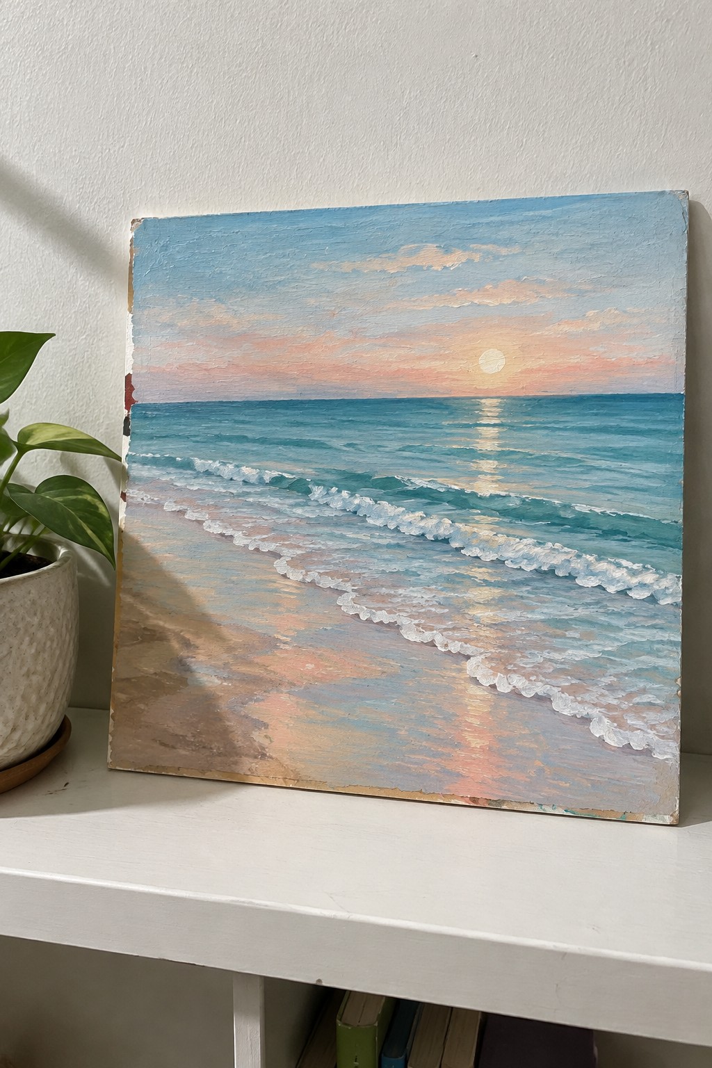 Seascape painting of sunset over turquoise waves on sandy beach beside potted plant