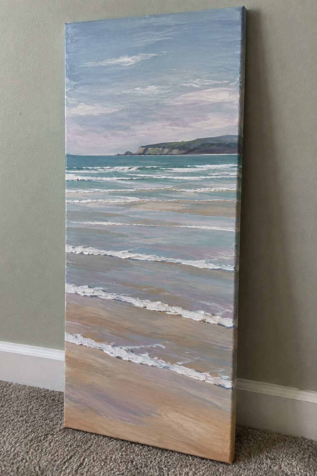Tall seascape painting of ocean waves, sandy beach and cliffs leaning on wall