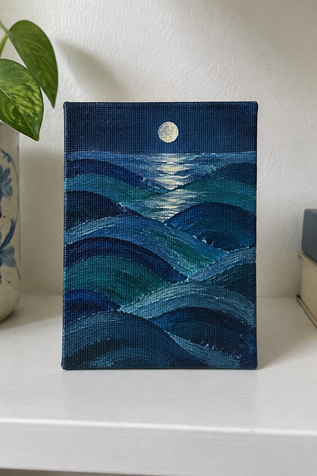 Painting of layered blue-green ocean waves under glowing moon on white shelf