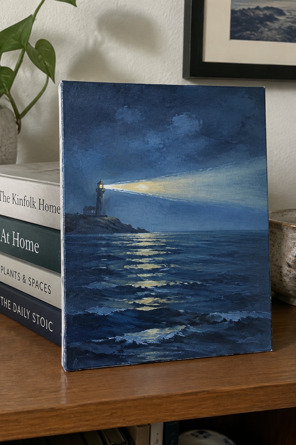 Dark blue lighthouse painting with glowing beam over reflective ocean waves on shelf