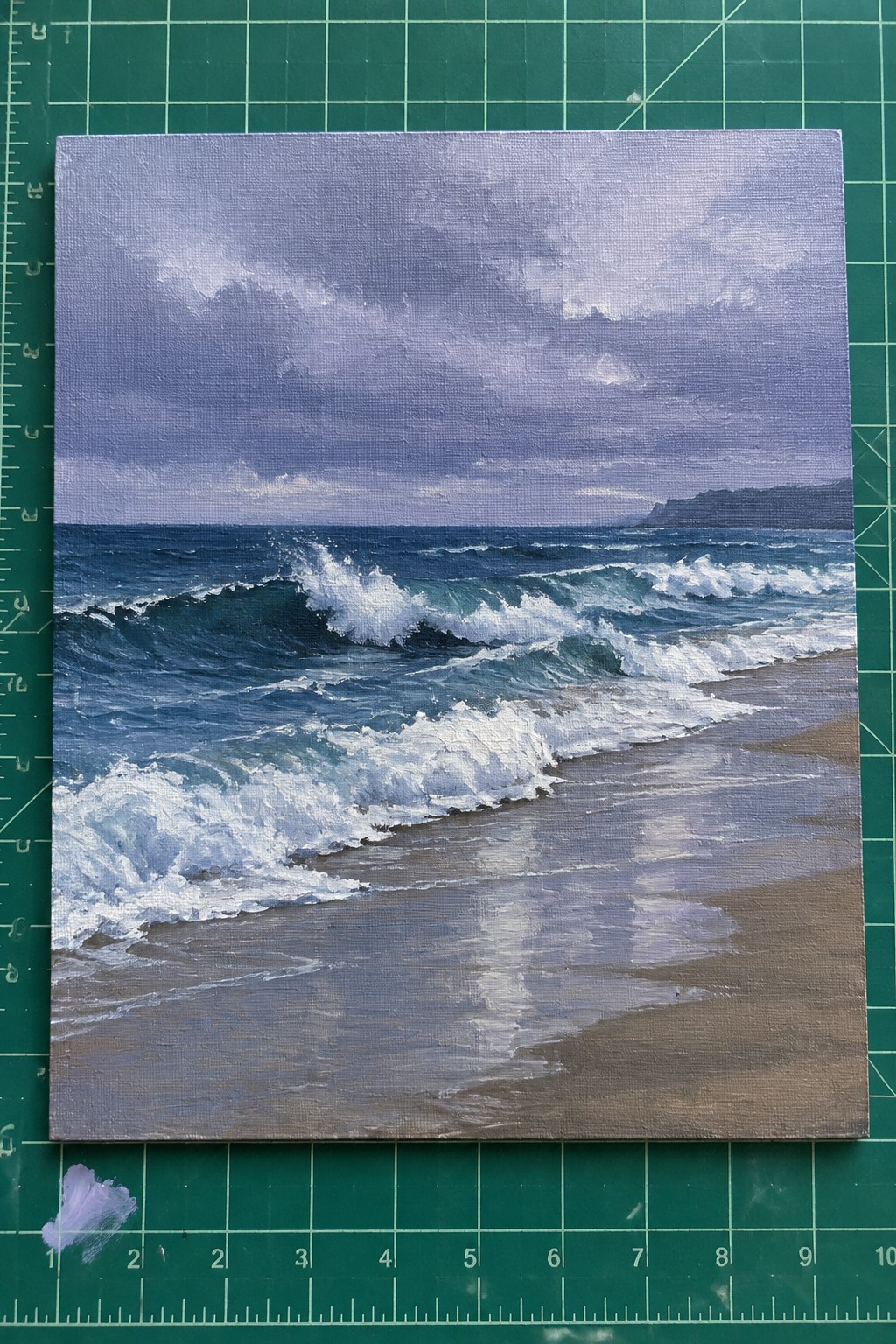 Seascape painting of crashing waves on wet sand beach atop green cutting mat