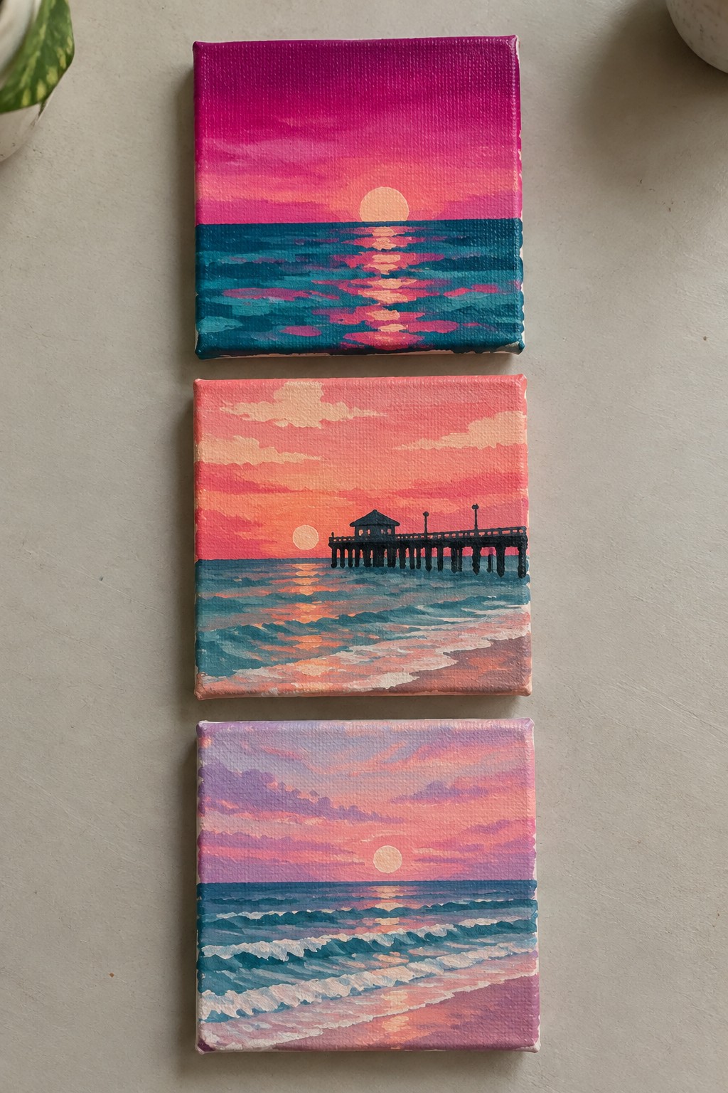 Three stacked miniature canvases of vibrant ocean sunsets with pier
