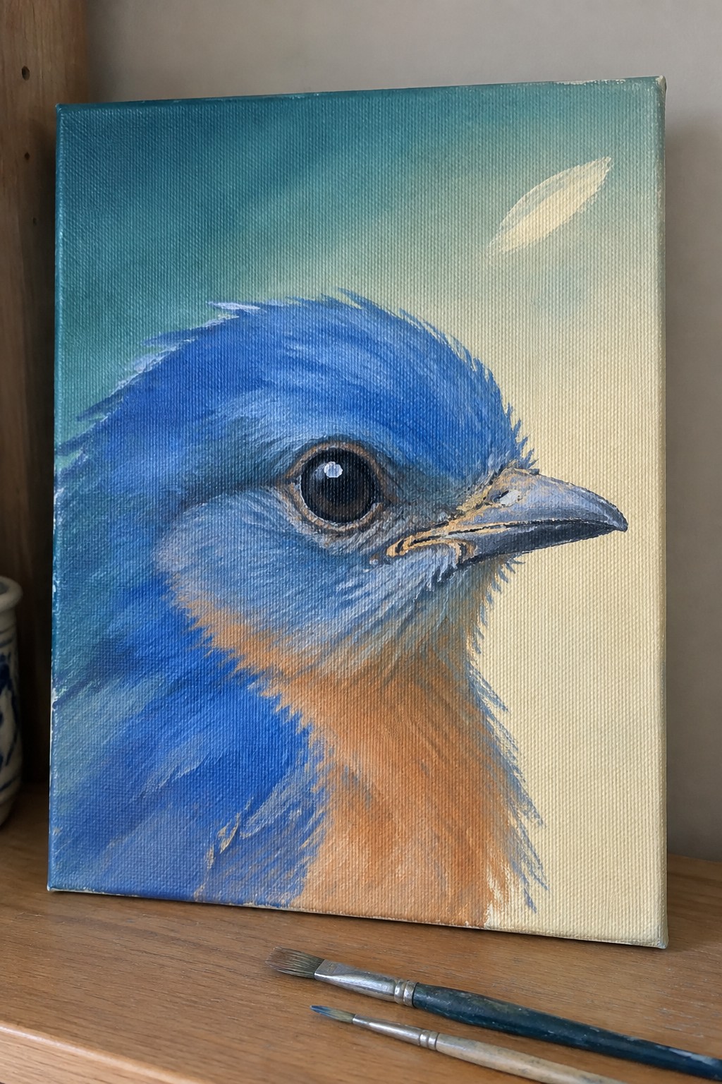 Bluebird painting on canvas with orange chest and paintbrushes on wood