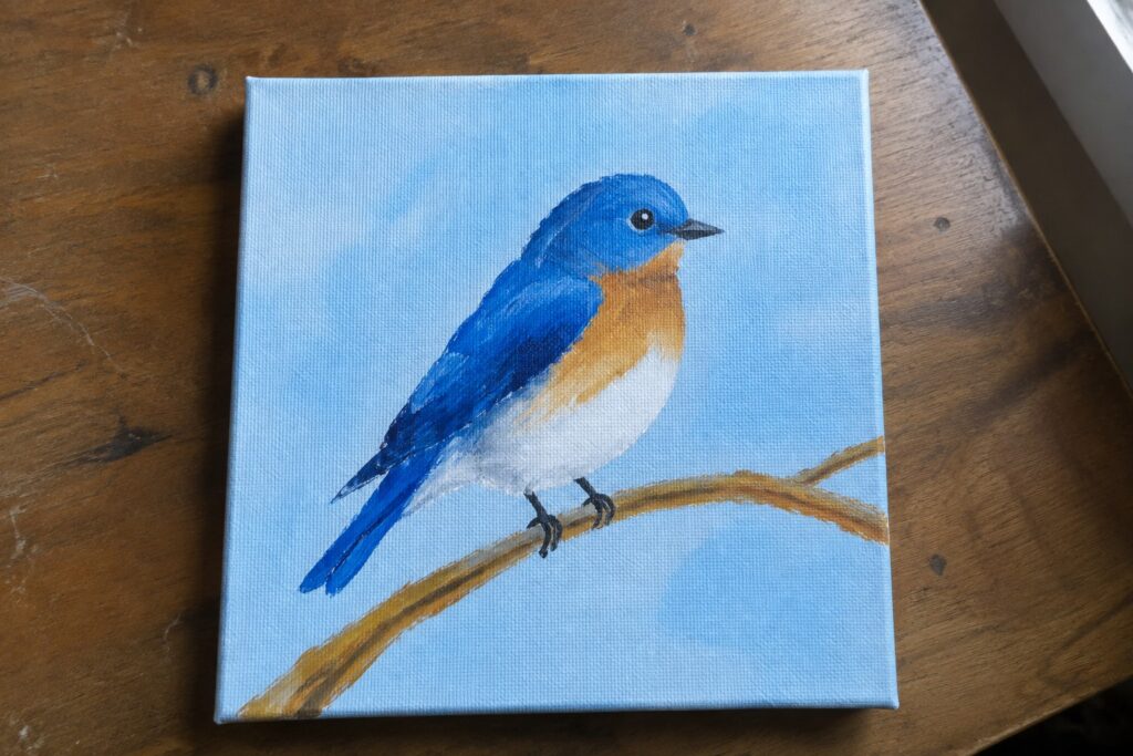 Bluebird with blue head and wings, orange breast, perched on branch against light blue background