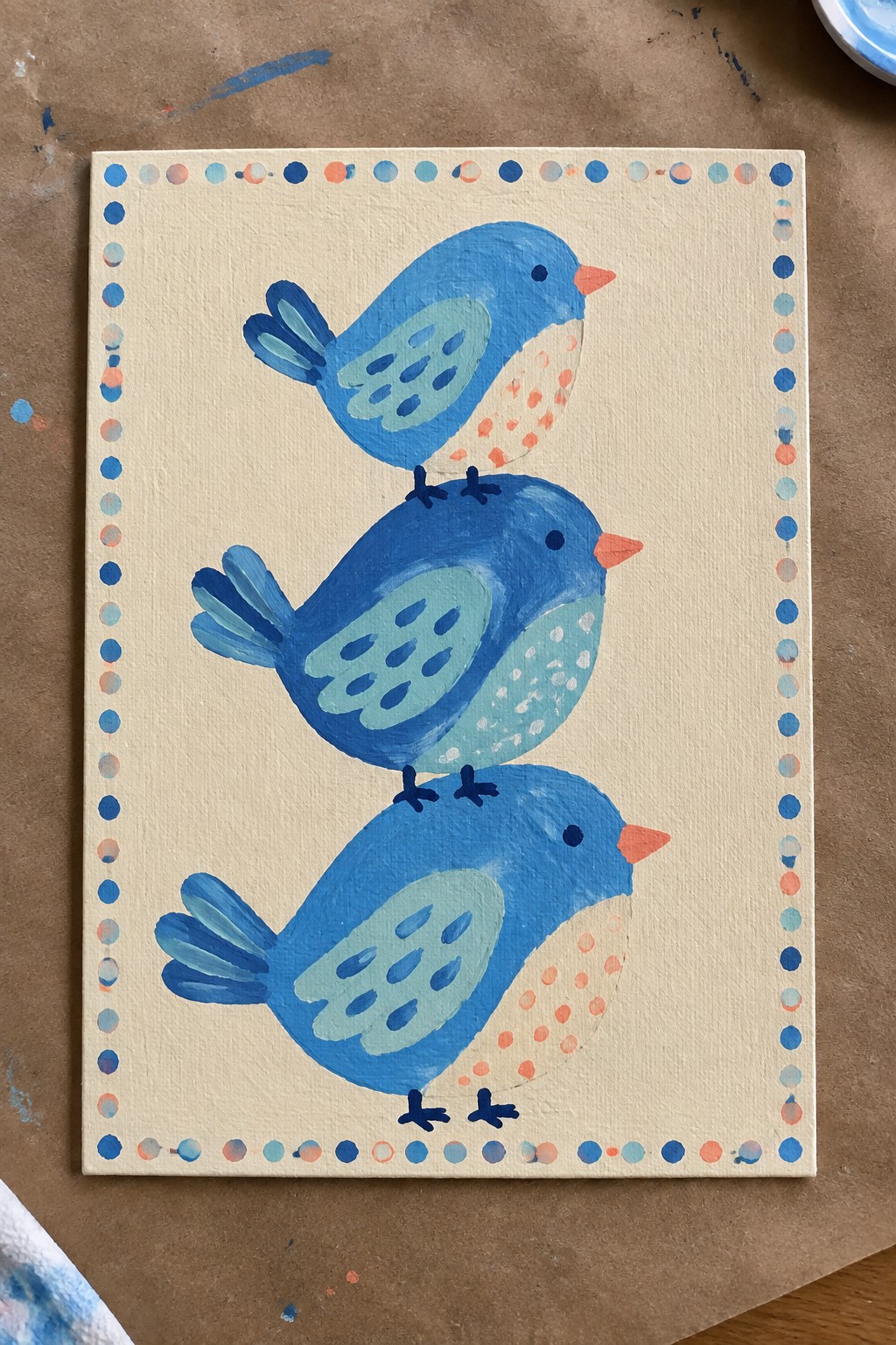 Three stacked blue birds on cream canvas with dotted blue-orange border