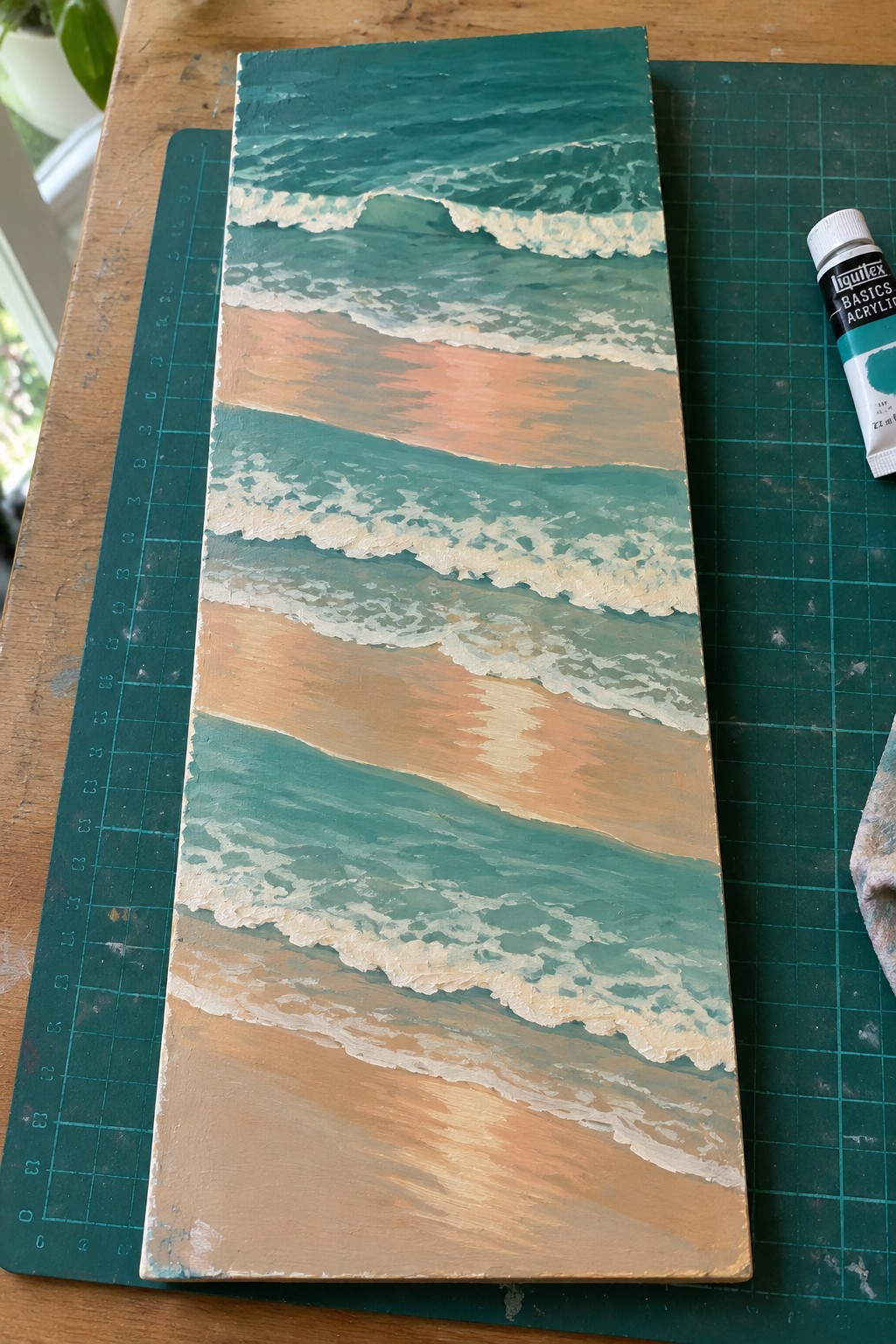Teal ocean wave painting with white foam over peach sand on wood panel