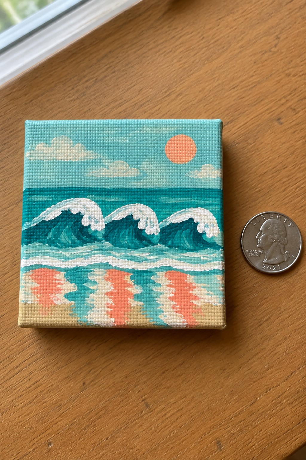 Miniature canvas painting of turquoise waves under orange sun beside quarter.