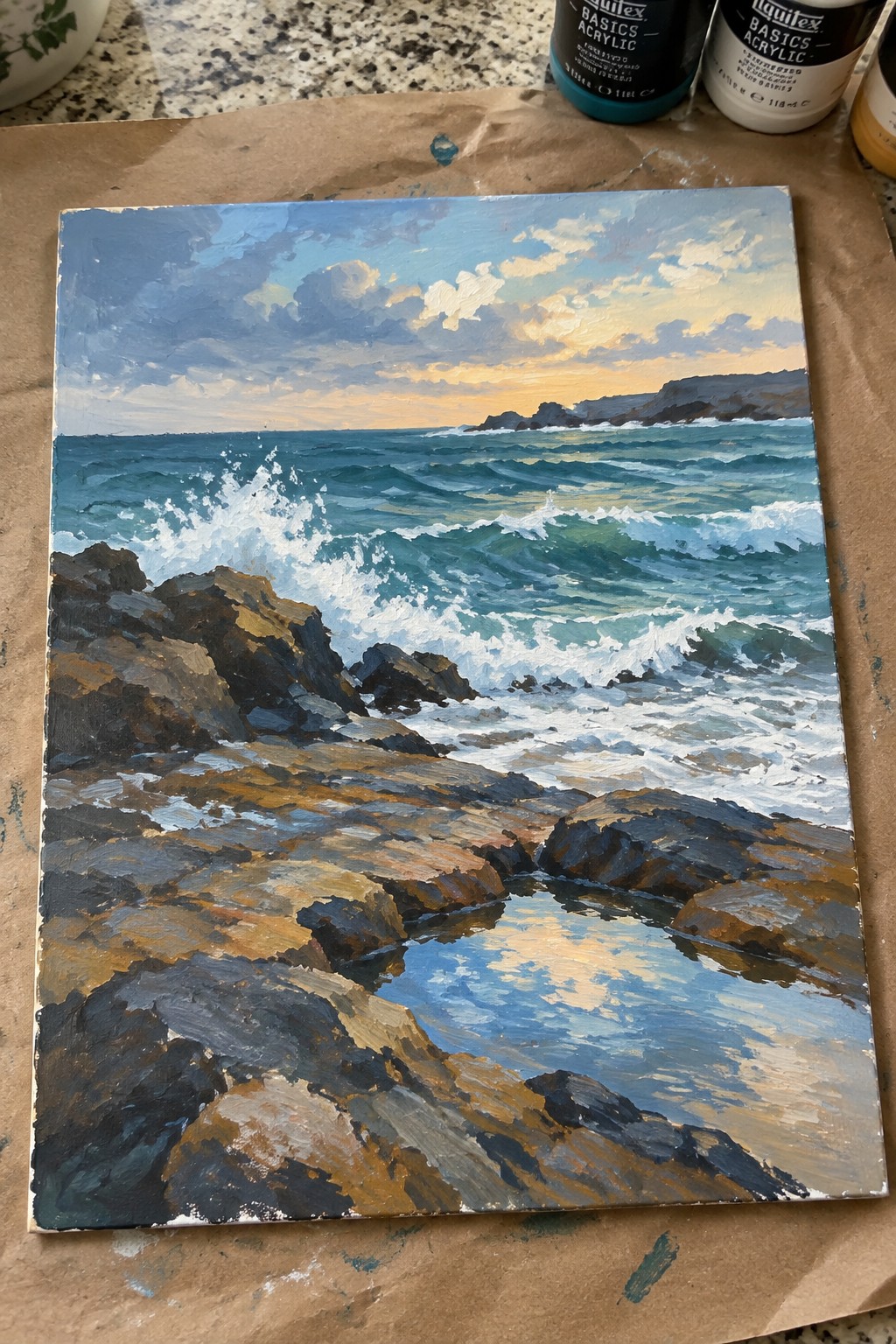 Acrylic painting of ocean waves breaking on dark rocks with a sunset sky and a reflective tide pool in the foreground.