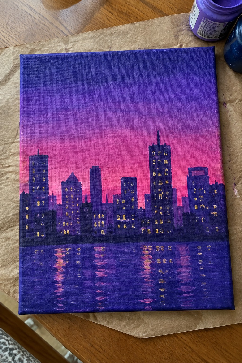 Purple-pink gradient sky over glowing city skyline painting with water reflections on canvas
