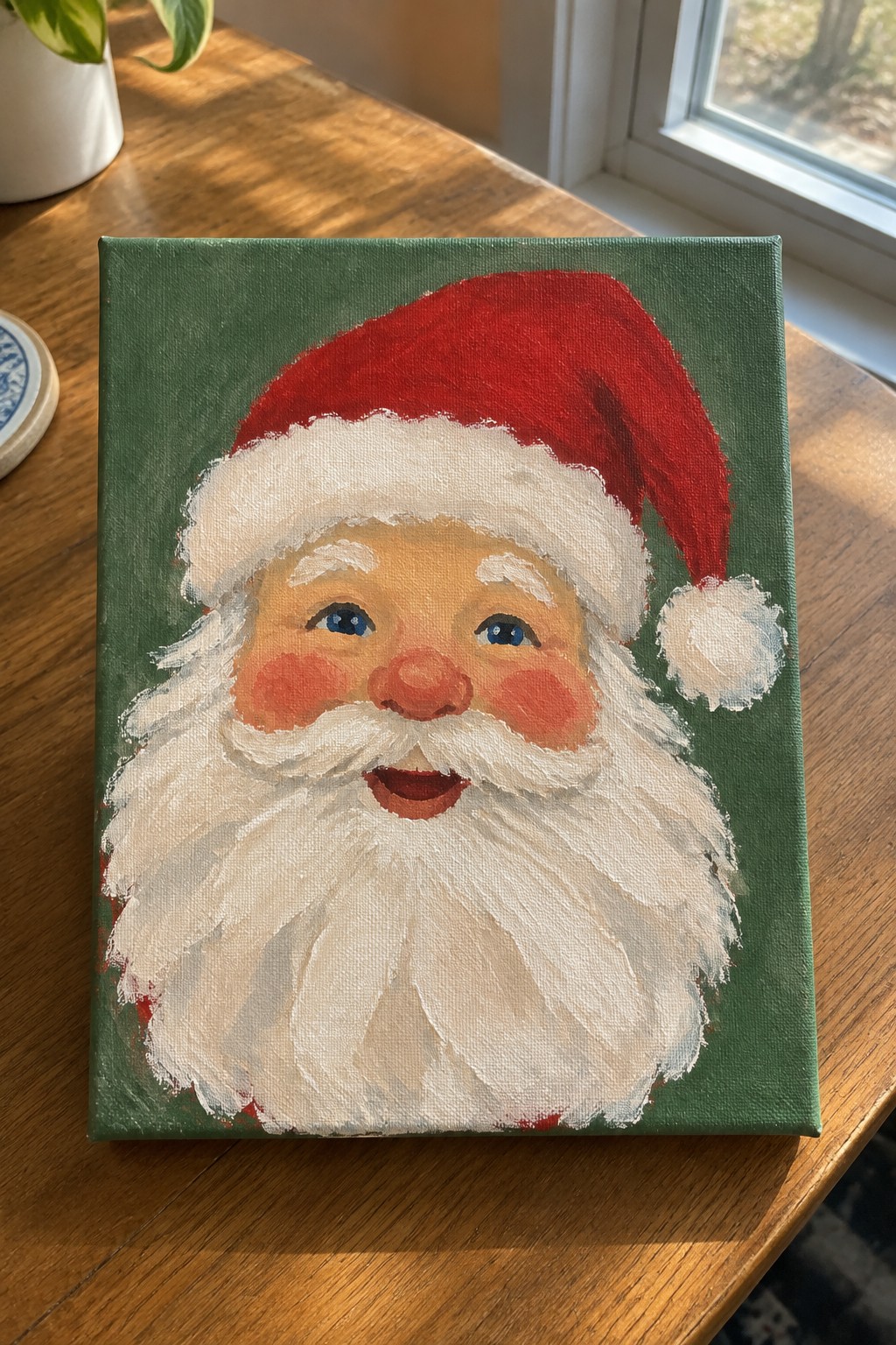 Santa Claus painting with red hat, white beard on green canvas atop wooden table