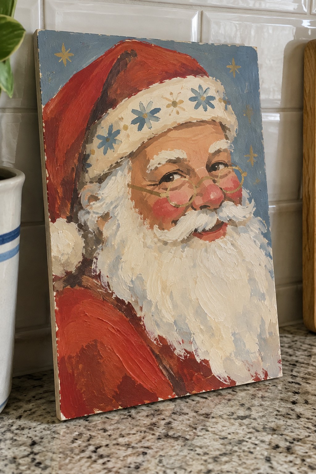 Thickly textured oil painting of Santa in red hat and gold glasses on granite counter.