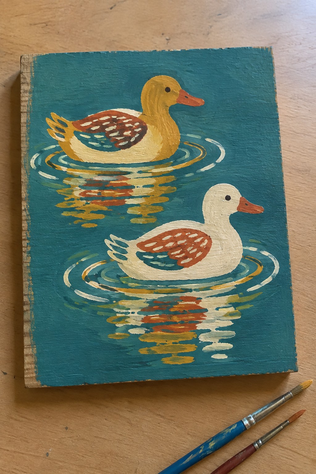 Two ducks swimming on rippled teal water with reflections and nearby paintbrushes.