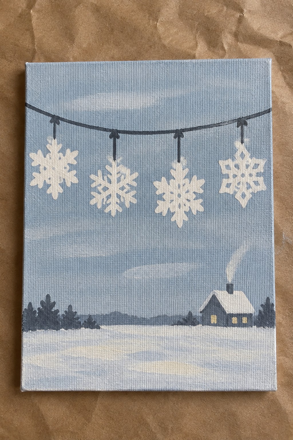 Light blue canvas painting of hanging snowflakes above snowy house with chimney smoke